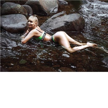 Blonde female posed lounging outdoors wearing bikini displaying rear