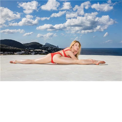 Blonde female posed wearing bikini doing split on beach