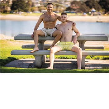 Two males posed topless seated outdoors wearing shorts