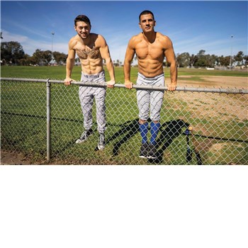 Two topless males posed outdoors on fence wearing jeans