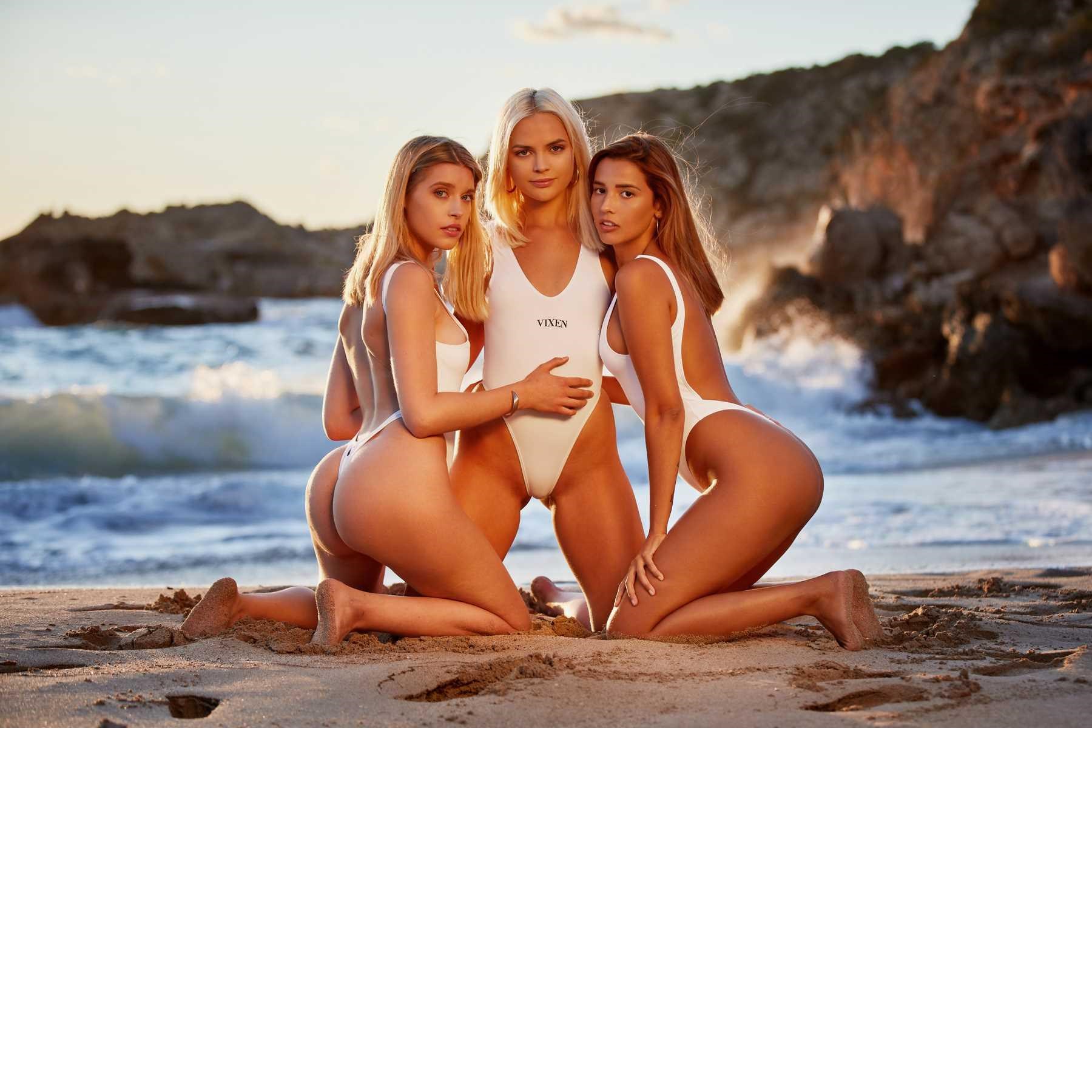 Three blonde females posed wearing swimsuits on beach