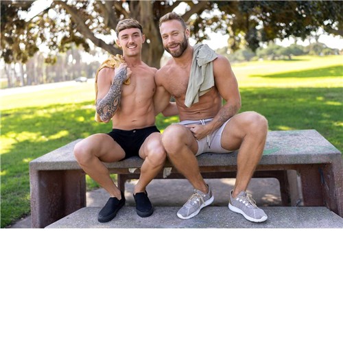 Two topless males posed seated caressing outdoors